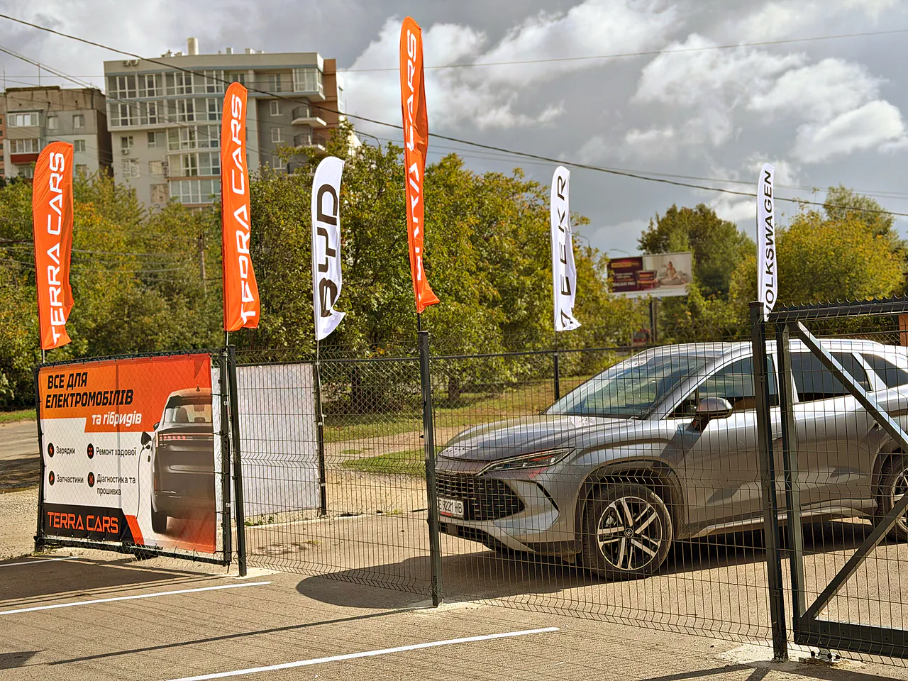 Сріблястий кросовер на майданчику Terra Cars біля прапорів і банера